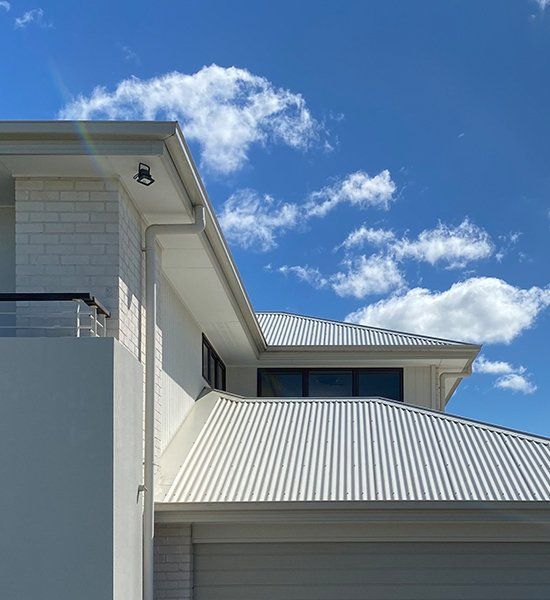 A White House With A White Roof And A Blue Sky In The Background — CP Roofing in Old Bar, NSW