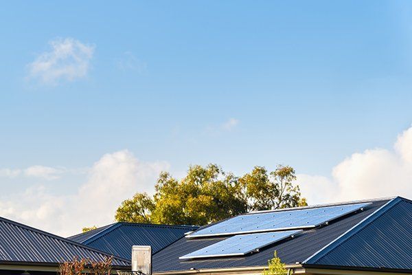 A House With Solar Panels On The Roof On A Sunny Day — CP Roofing in Taree, NSW