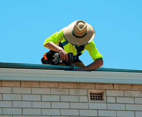 A Man Wearing A Hat Is Working On The Roof Of A Building — CP Roofing in Wingham, NSW