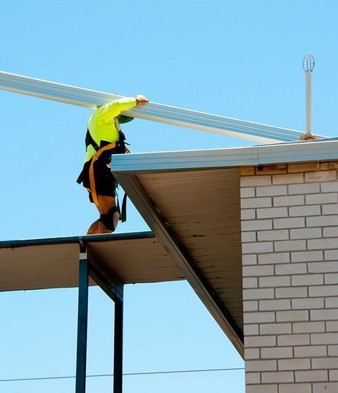 A Man Is Working On The Roof Of A Building — CP Roofing in Wingham, NSW