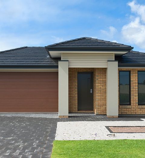 A Brick House With A Black Roof And A Brown Garage Door — CP Roofing in Old Bar, NSW