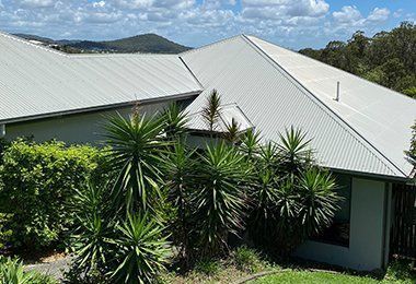 A White House With A White Roof Is Surrounded By Trees And Bushes — CP Roofing in Old Bar, NSW