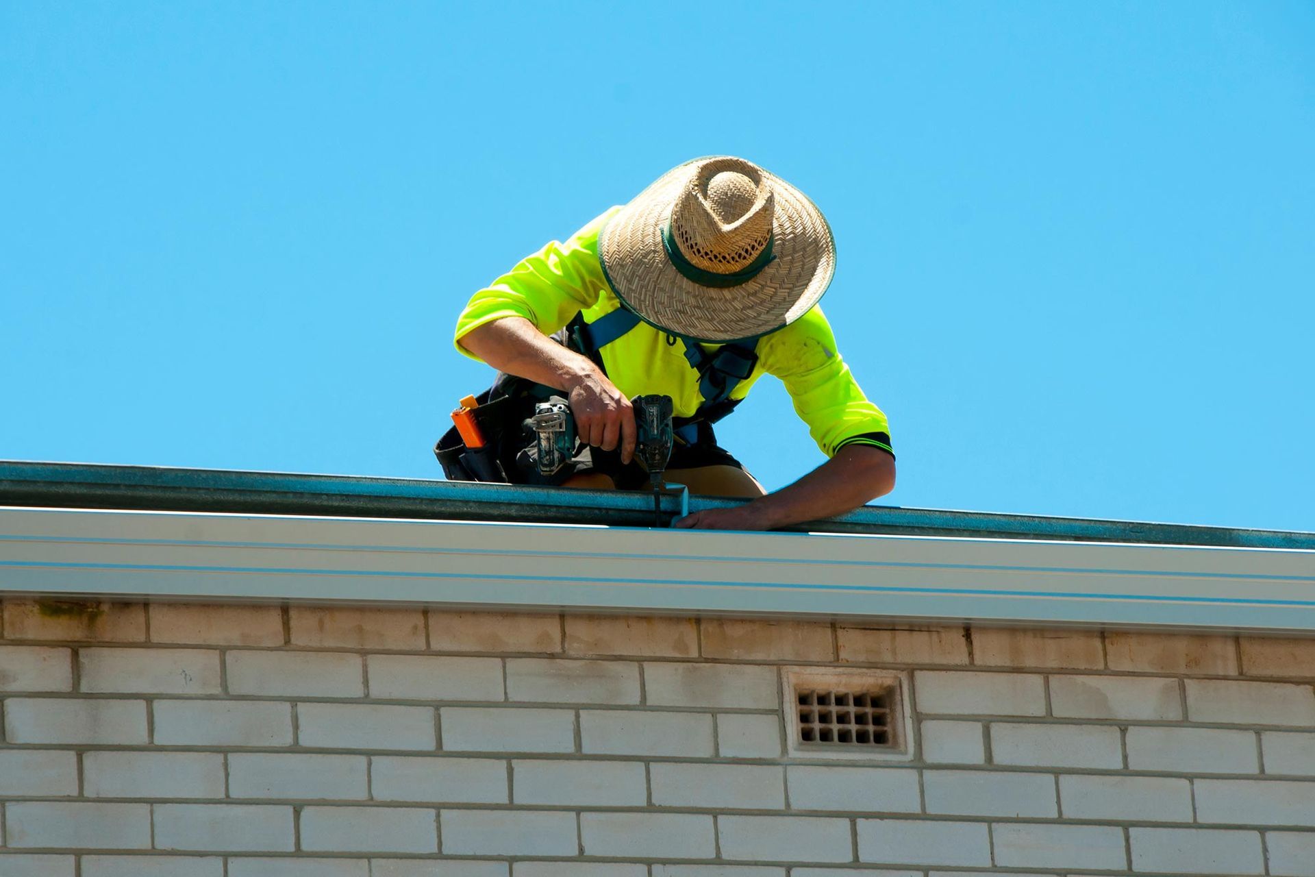 A Man In A Straw Hat Is Working On The Roof Of A Building — CP Roofing in Old Bar, NSW