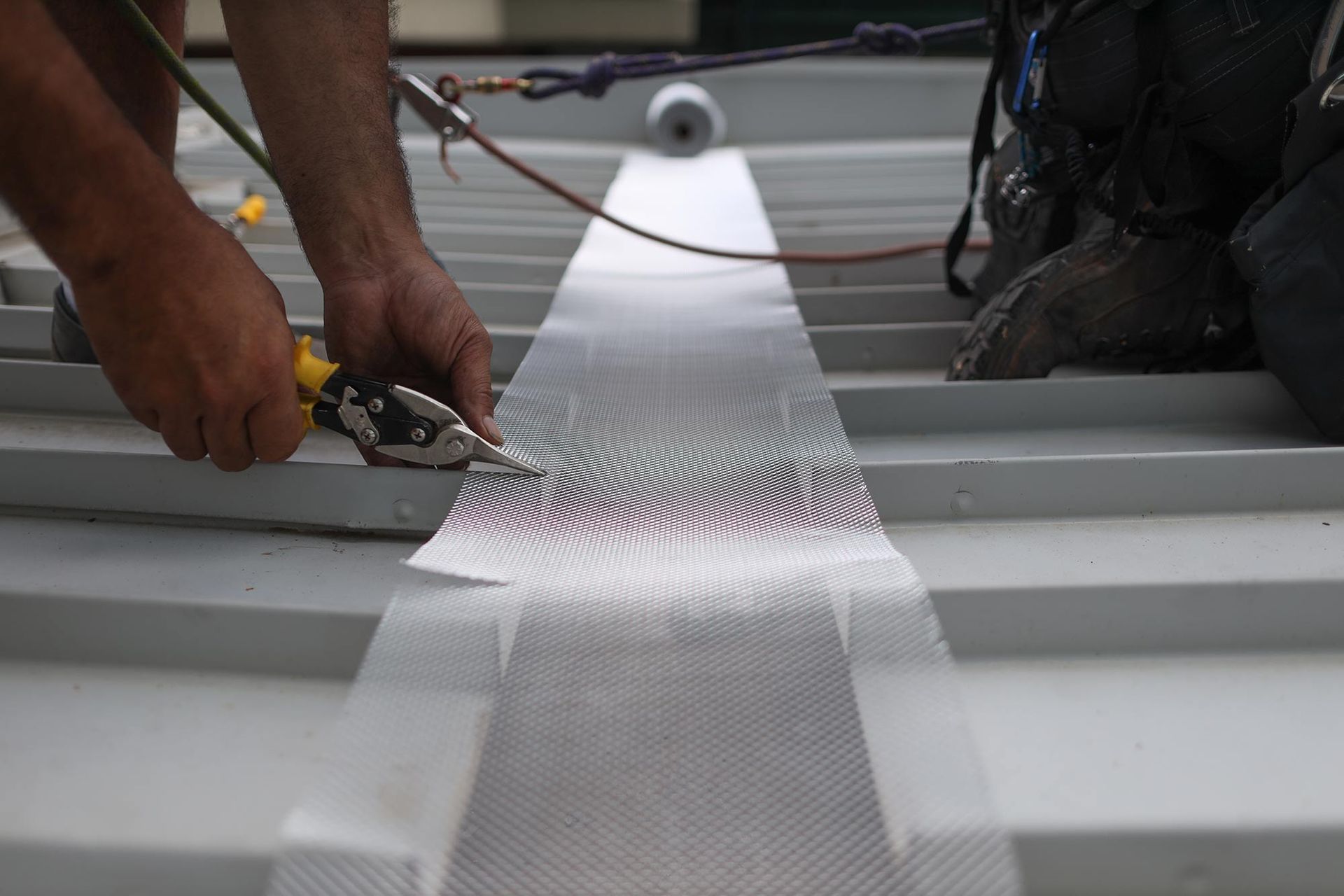 A Man Is Working On A Roof With A Pair Of Pliers — CP Roofing in Gloucester, NSW