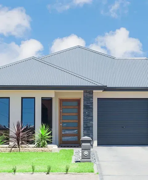 The Front Of A House With A Blue Roof And A Black Garage Door — CP Roofing in Taree, NSW