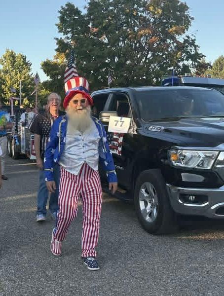 Uncle Sam in costume walking in a parade next to a black truck.