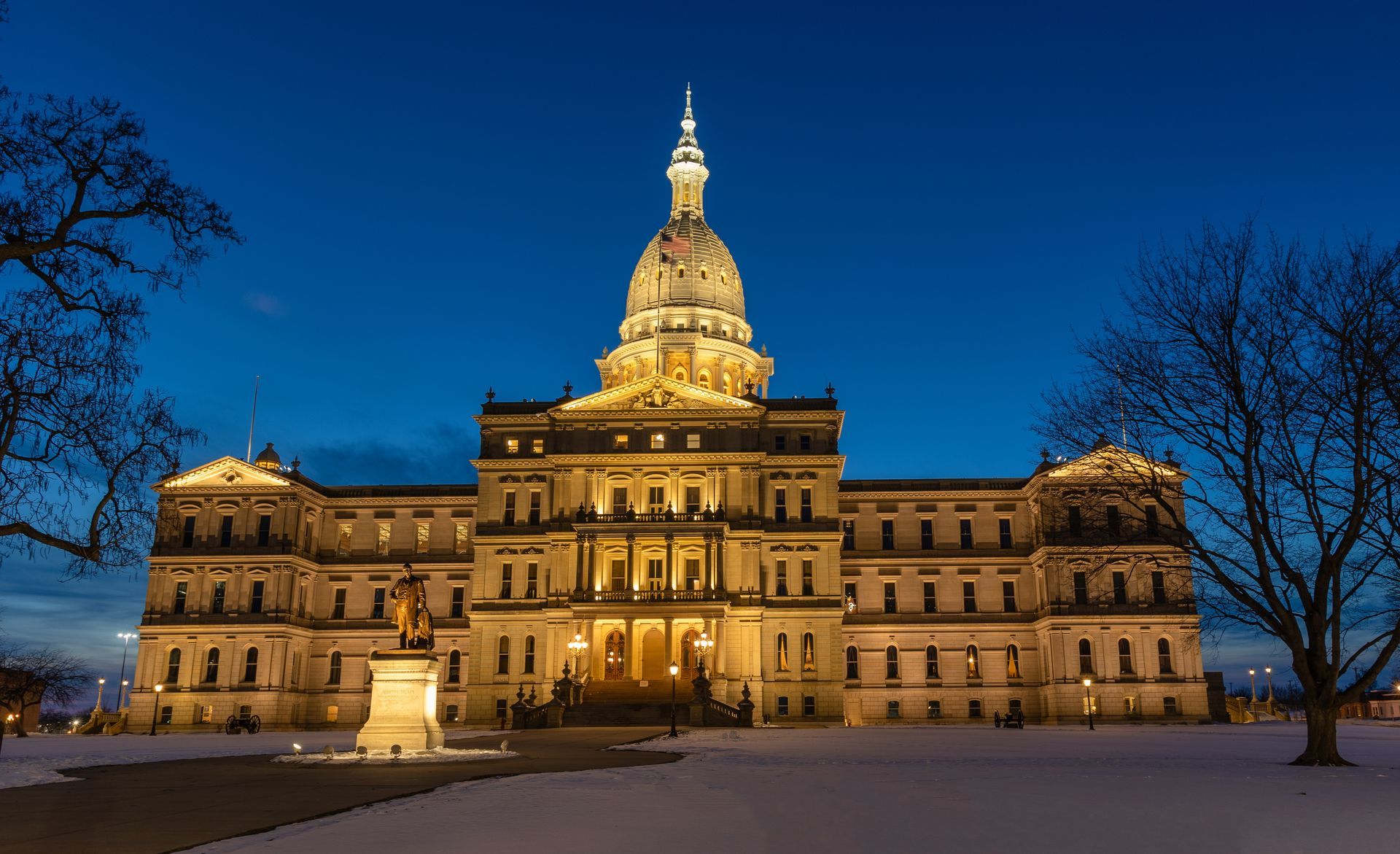 Michigan State Capitol building lit up at dusk. Snow on the ground.