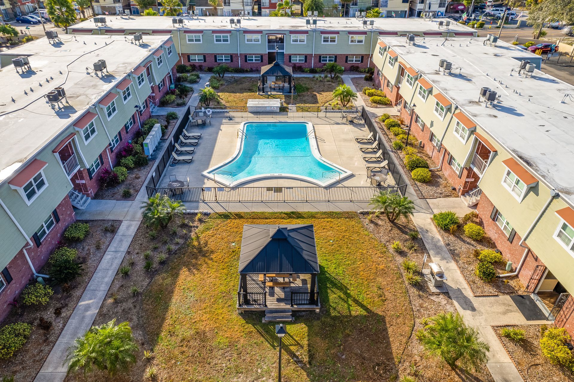 Aerial view of an apartment complex with a pool, gazebo, and surrounding buildings with red brick and green accents.