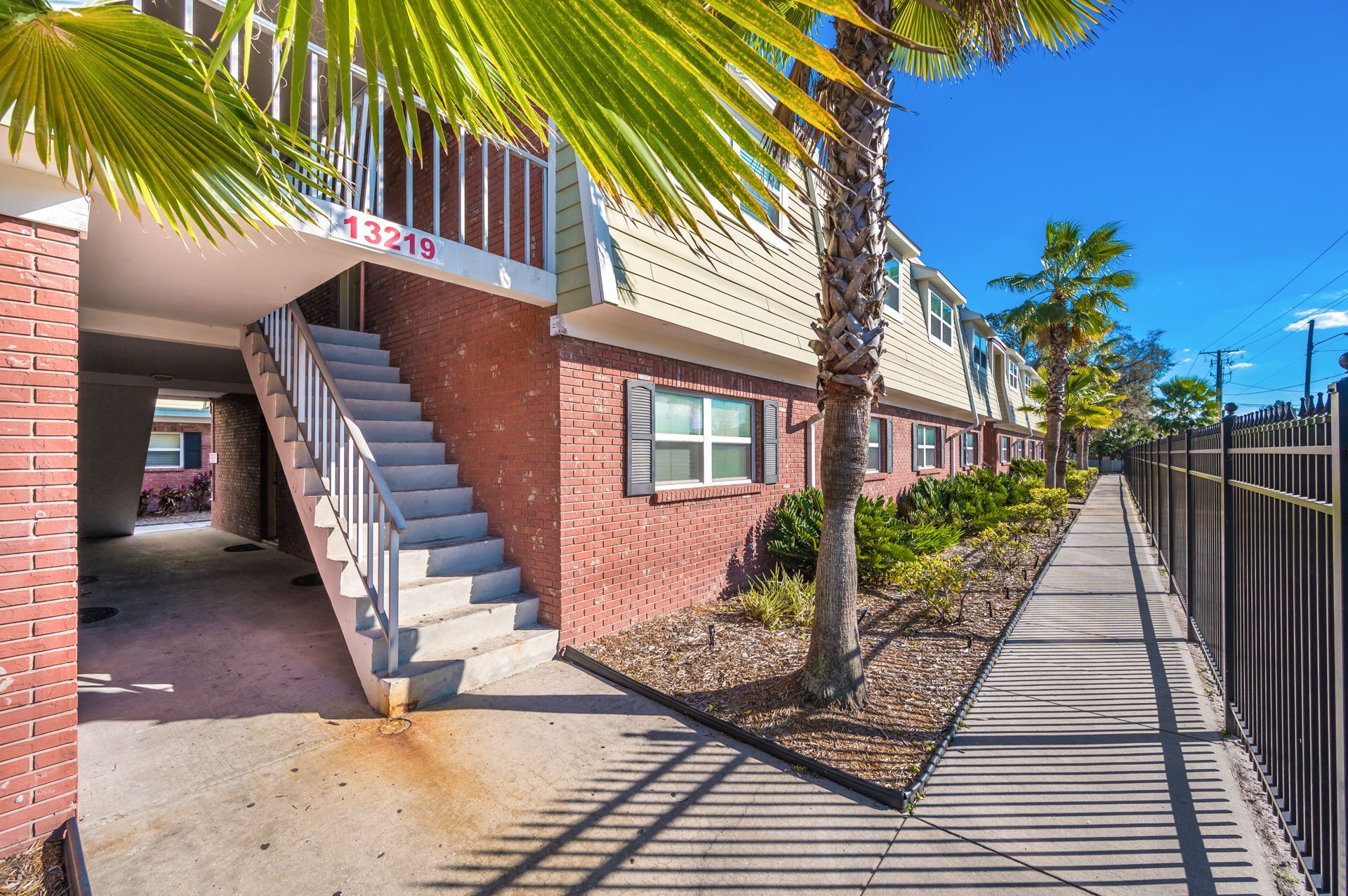 Building exterior with stairs, brick facade, and palm trees on a sunny day.