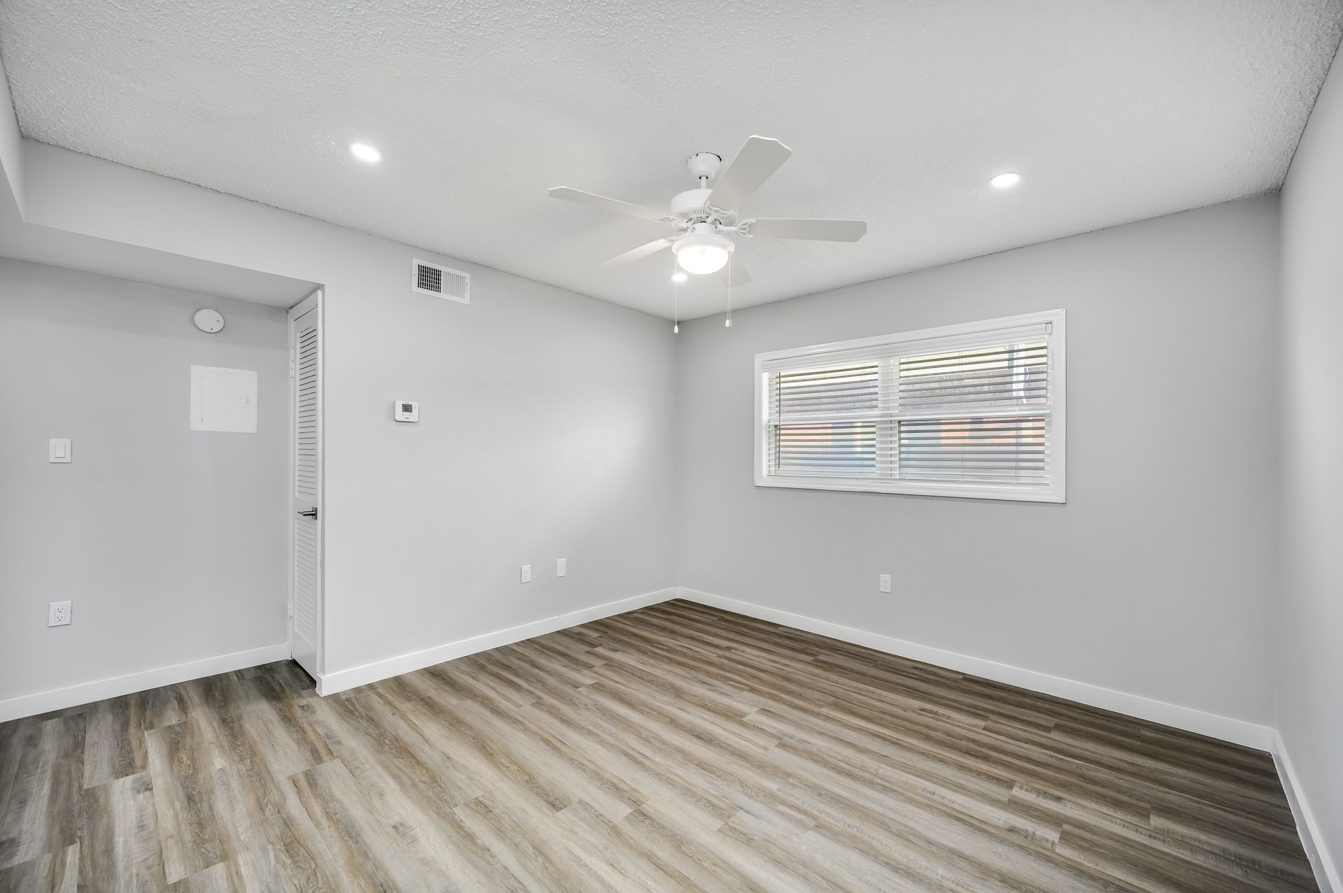 Empty bedroom with gray walls, wood-look flooring, ceiling fan, and window.
