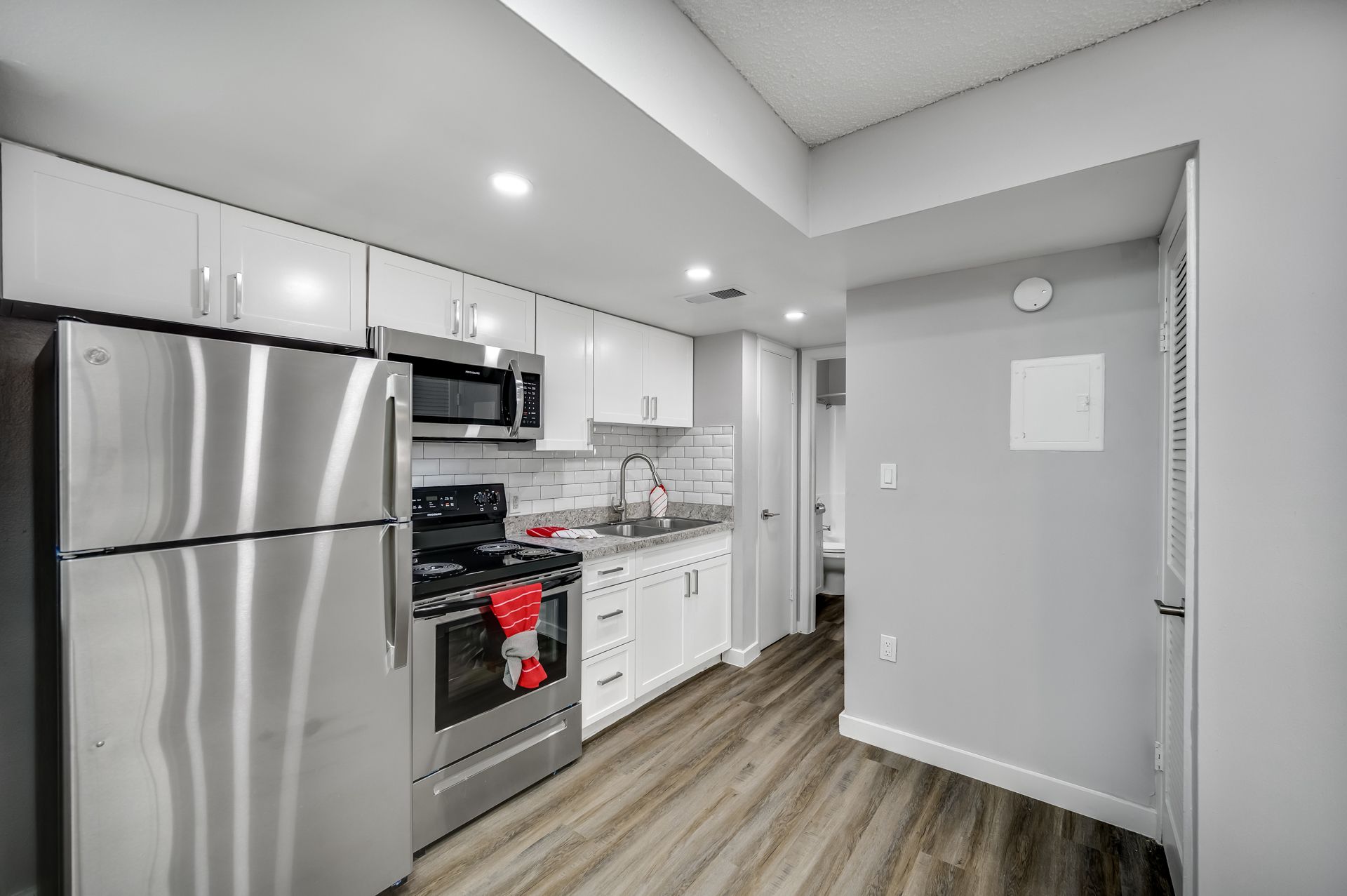 Modern kitchen with stainless steel appliances, white cabinets, and light wood-look flooring.