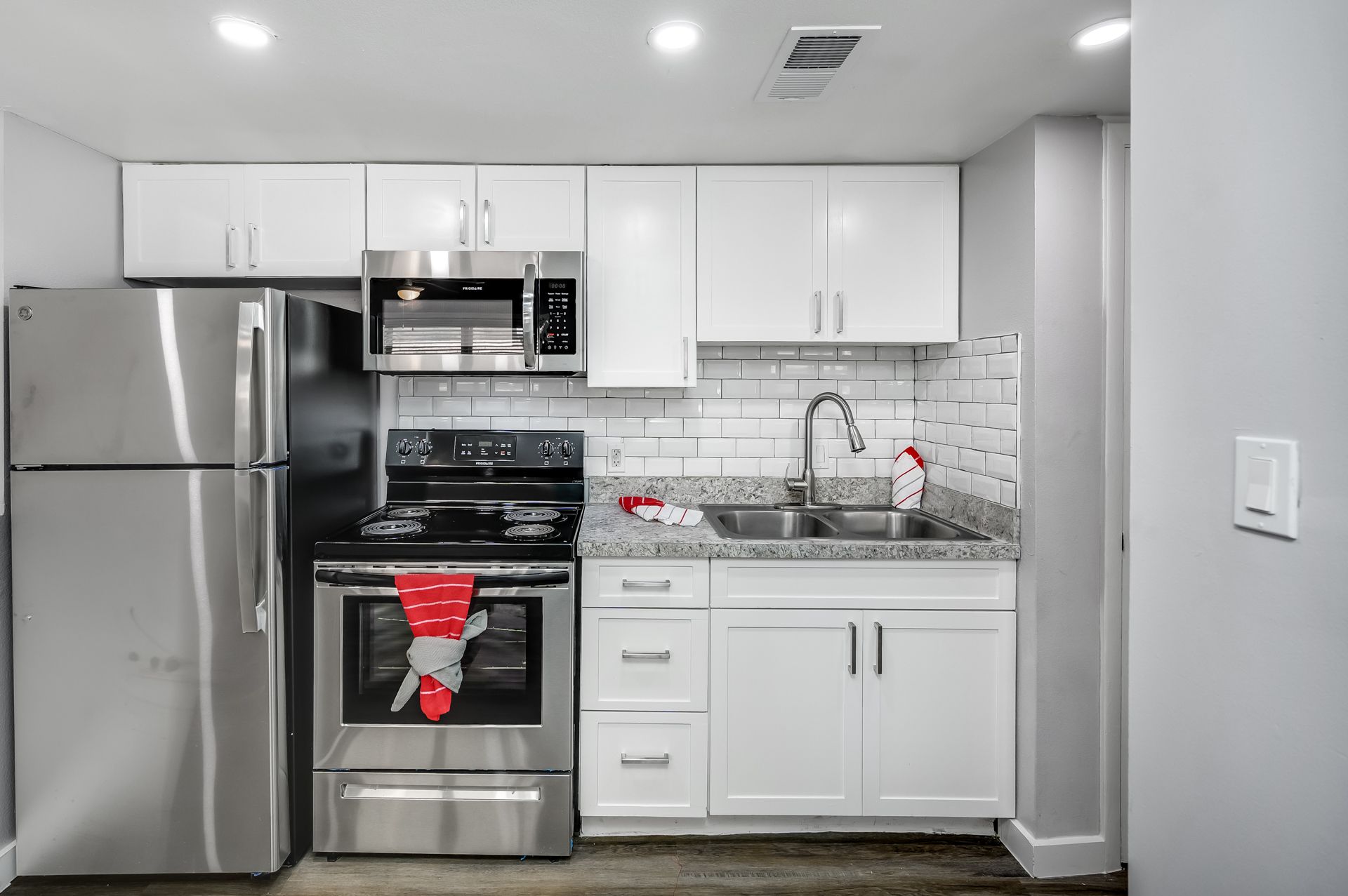 Small, modern kitchen with white cabinets, stainless steel appliances, and a brick-pattern backsplash.