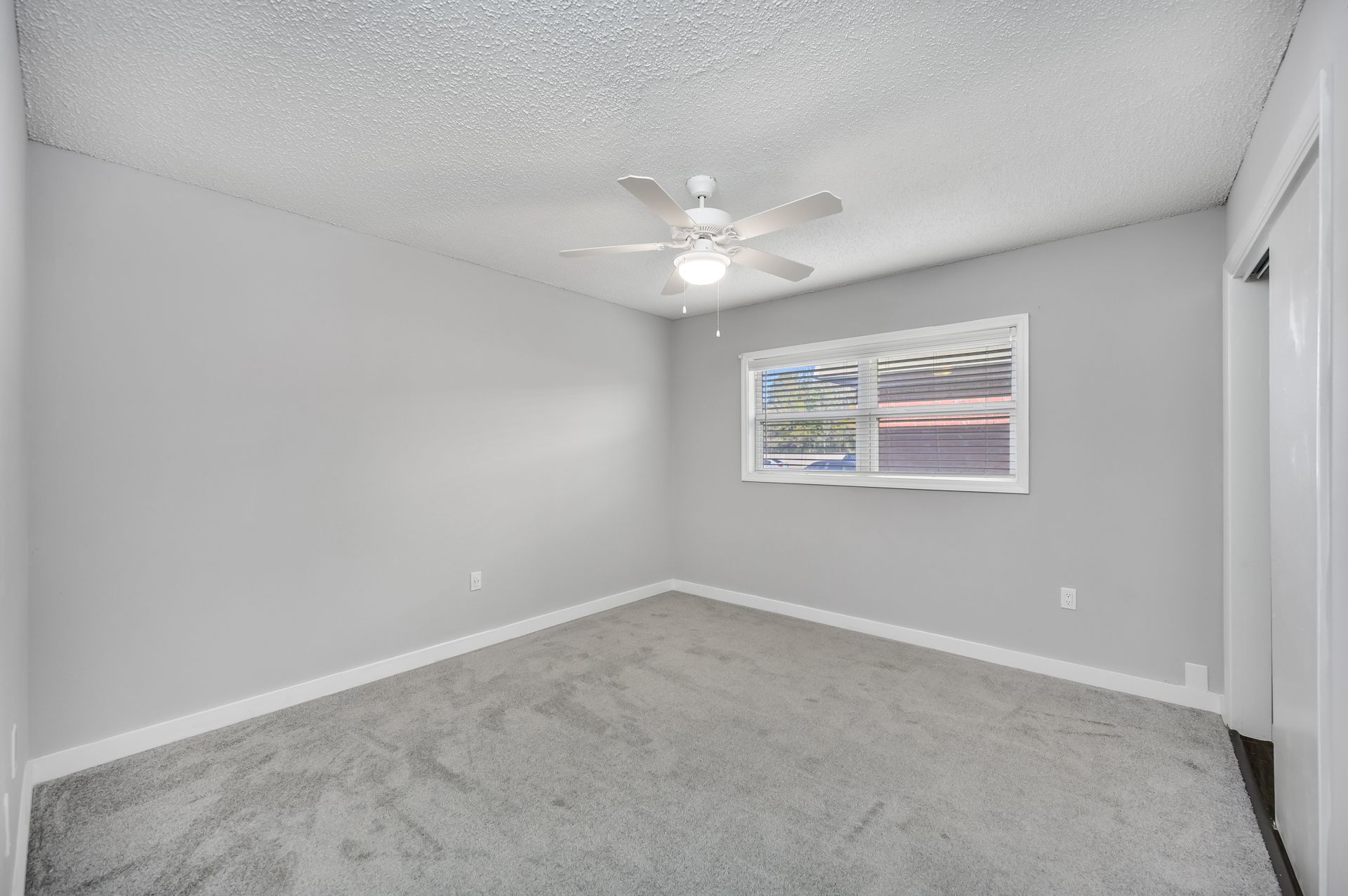 Empty bedroom with gray walls, carpet, ceiling fan, and window.