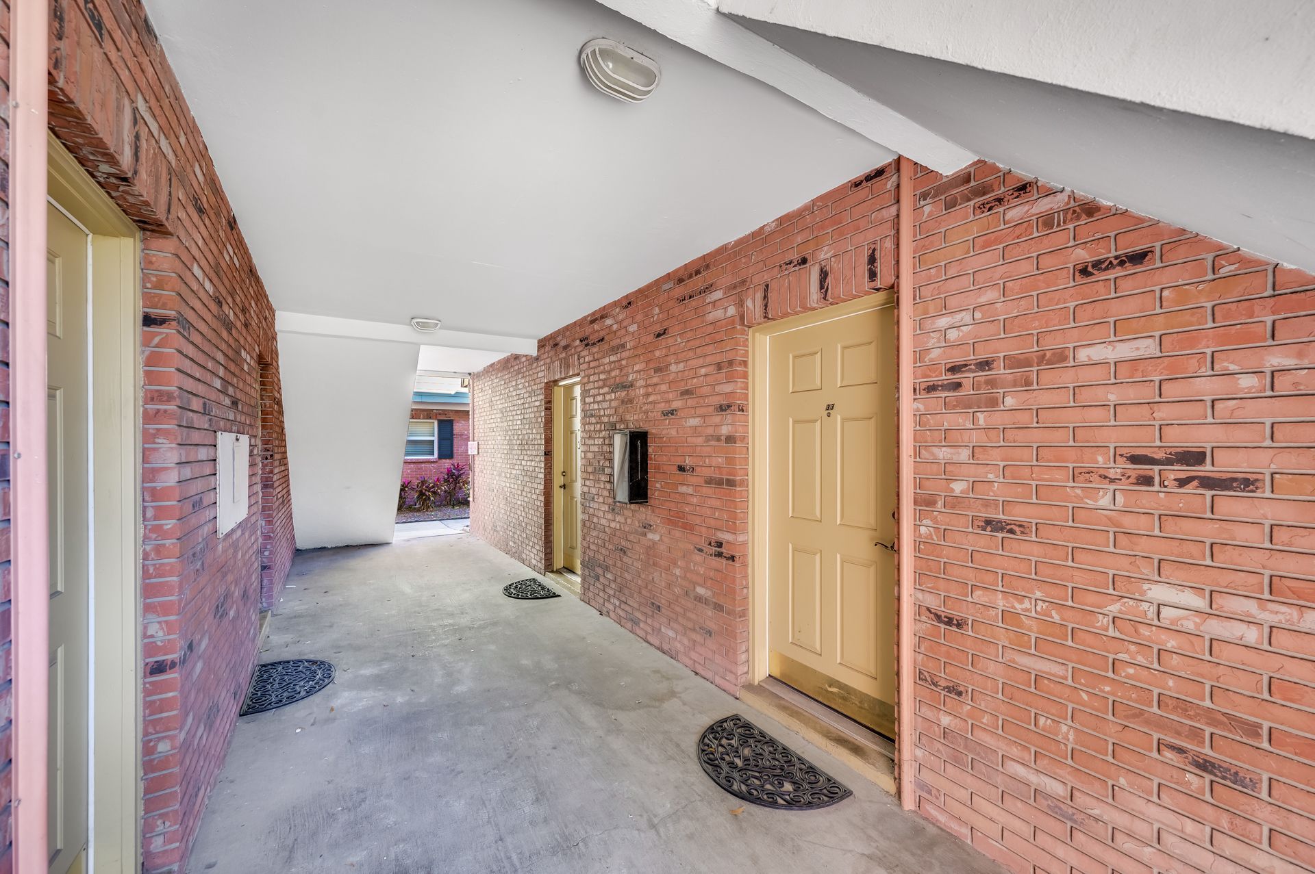 Brick hallway with doors, overhead lighting, and concrete flooring.