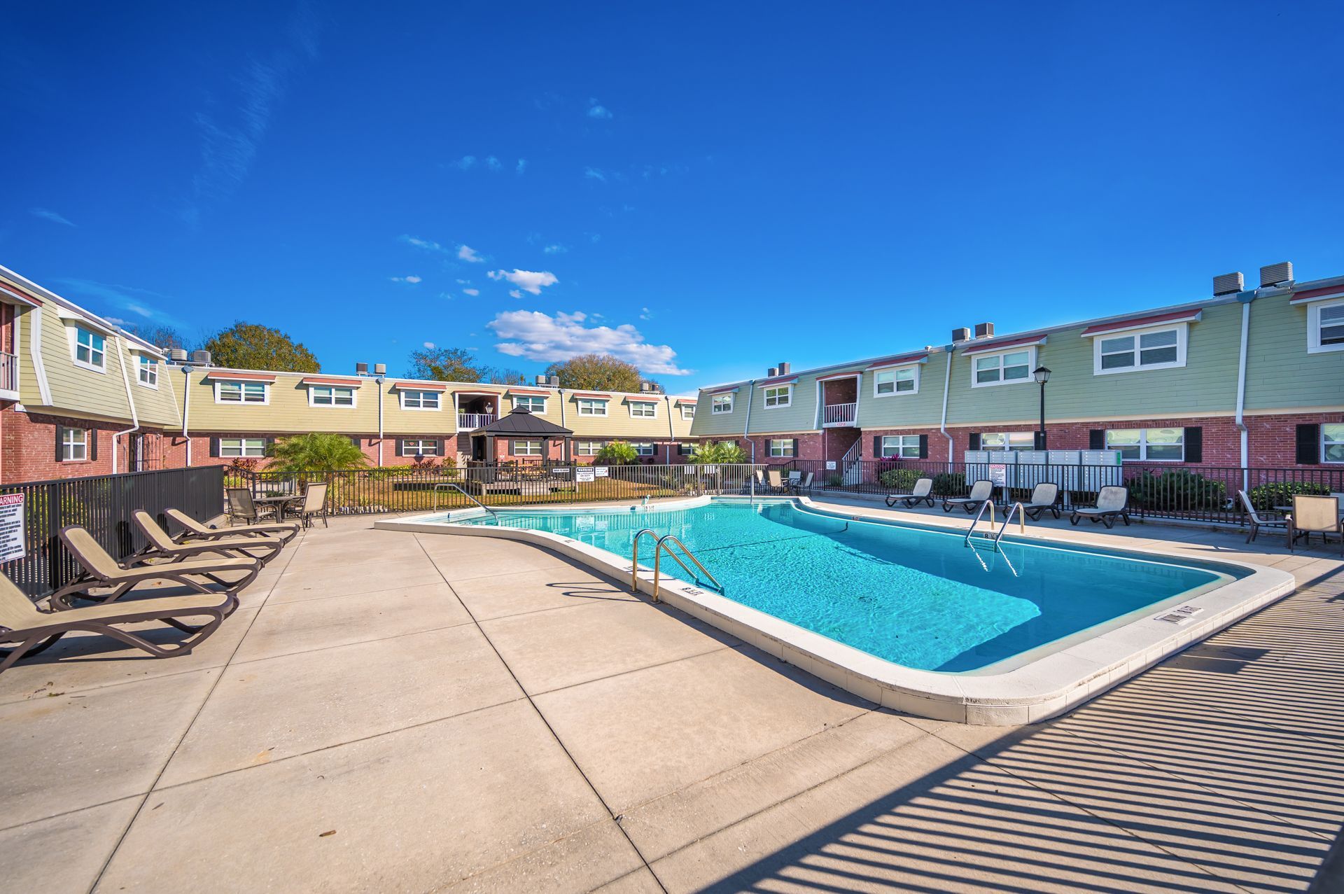 Swimming pool surrounded by townhouses, lounge chairs, and a gazebo on a sunny day.