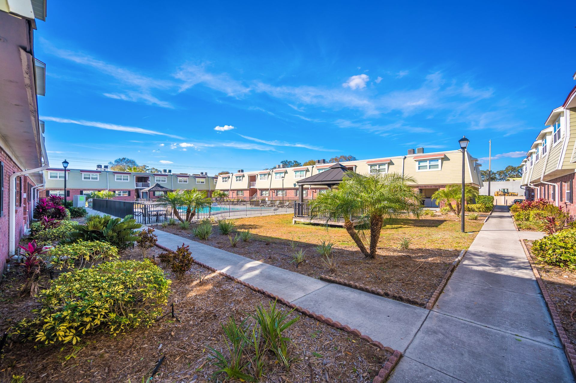 Courtyard of apartments with pool, landscaping, blue sky.