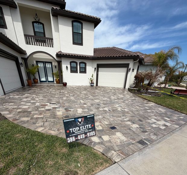 A two-story white house with a paved driveway featuring a promotional sign for Top Elite Pavers.