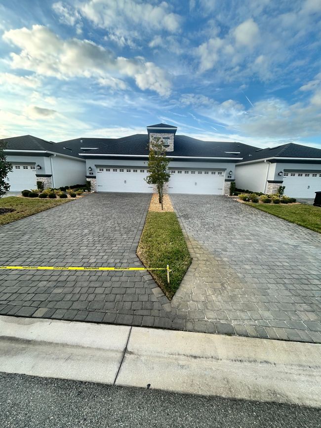 A paved driveway leads to a row of modern houses with white garage doors, separated by a narrow patch of grass.