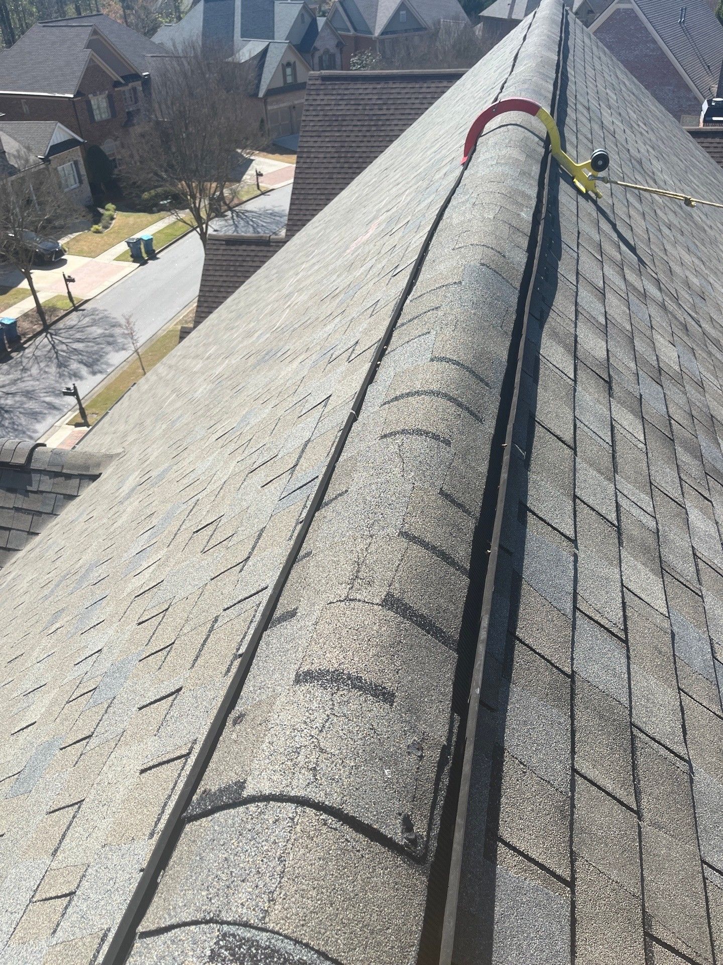 Close-up of a gray shingled roof ridge with safety harness and cityscape background.