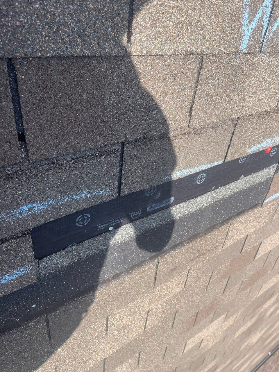 Close-up of asphalt roof shingles with a black strip of underlayment visible.