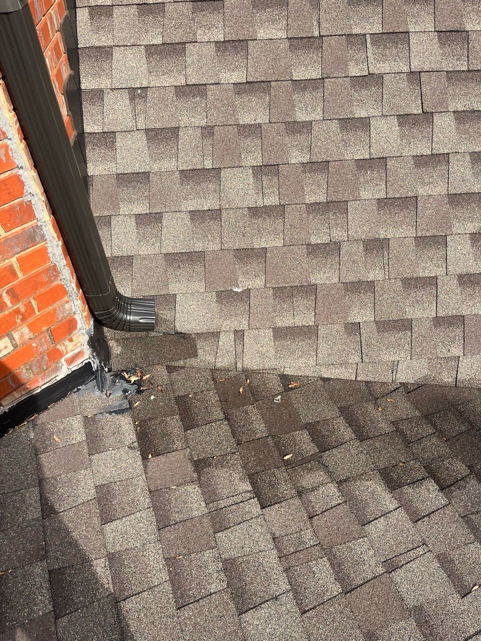Brown asphalt shingle roof with a black gutter; next to a red brick wall.