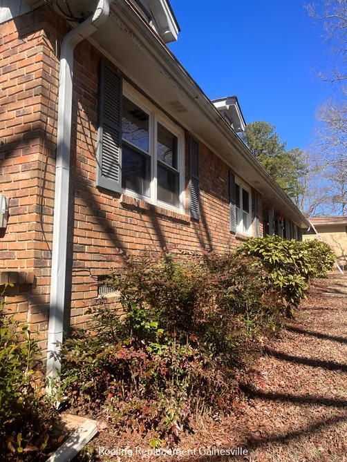 Brick house exterior with dark shutters, white trim, and bushes. Sunny day.