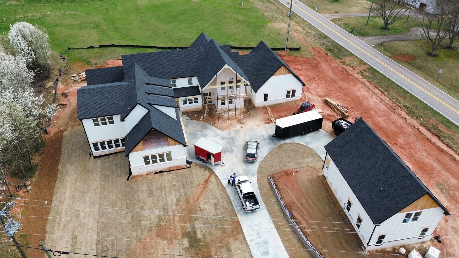 Aerial view of a large, modern home under construction with a long driveway and surrounding construction site.