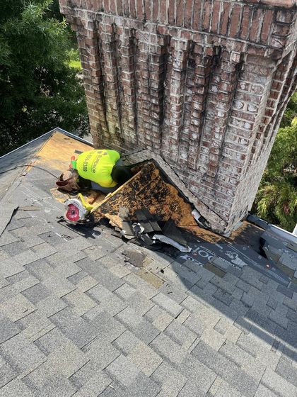 Chimney on roof with damaged flashing; debris and worker in yellow vest visible.