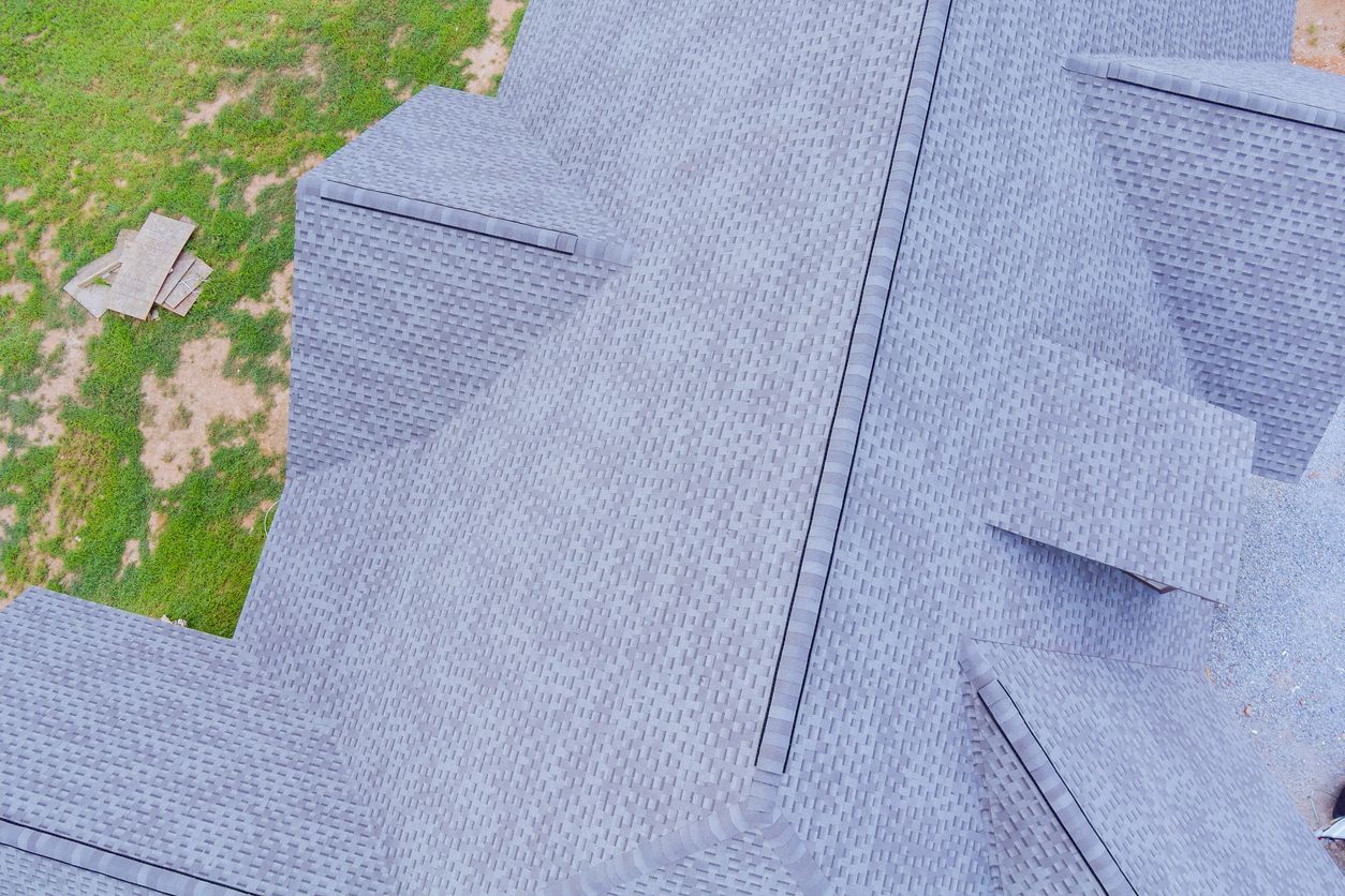 Overhead view of a gray shingled roof with a complex design against a green yard.