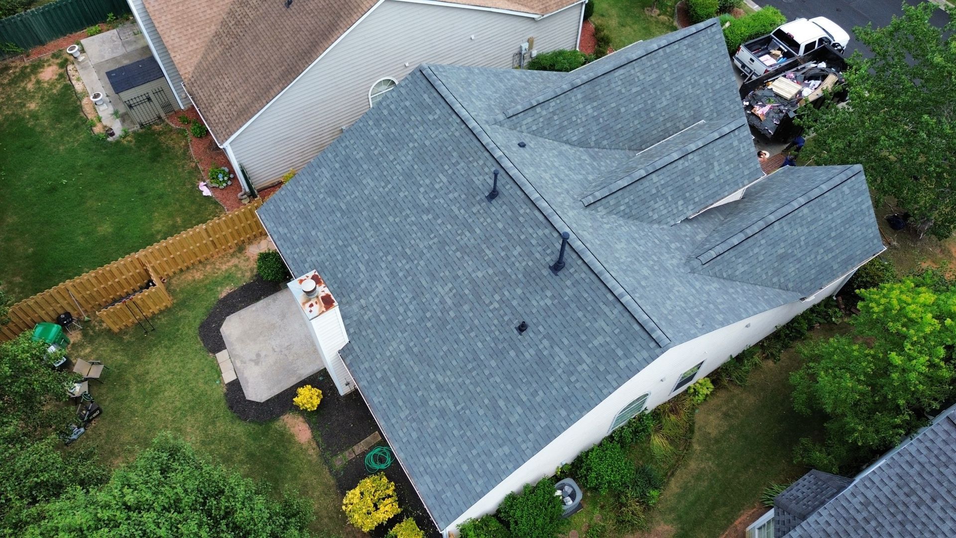 Overhead view of a house with a gray roof and white siding, surrounded by green grass and trees.