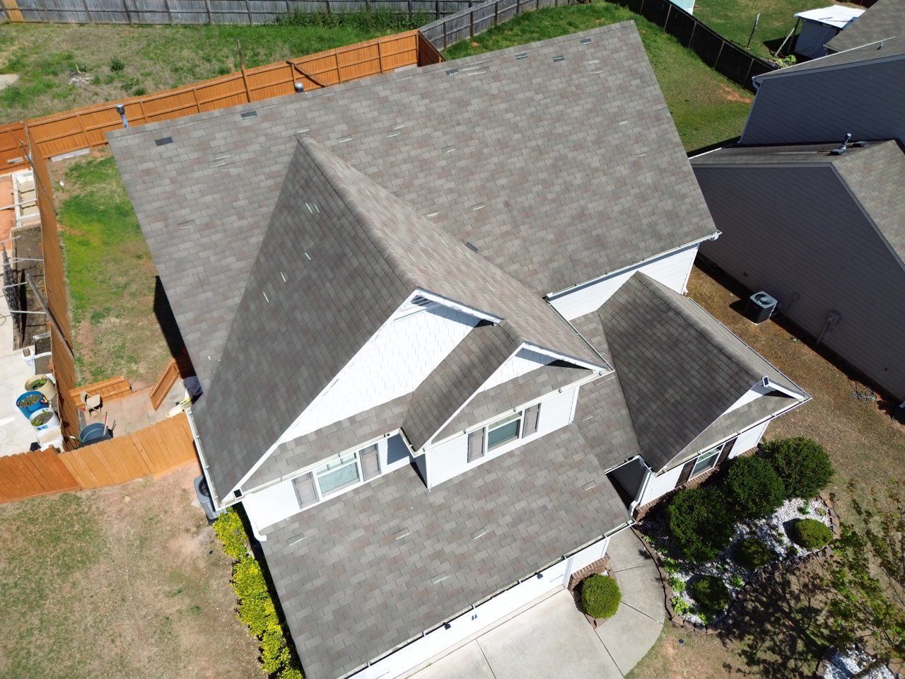Overhead view of a two-story house with a gray shingle roof, white siding, and a small backyard.