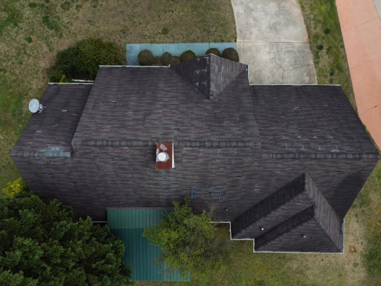 Aerial view of a dark shingled house roof with a chimney, satellite dish, and green accents.