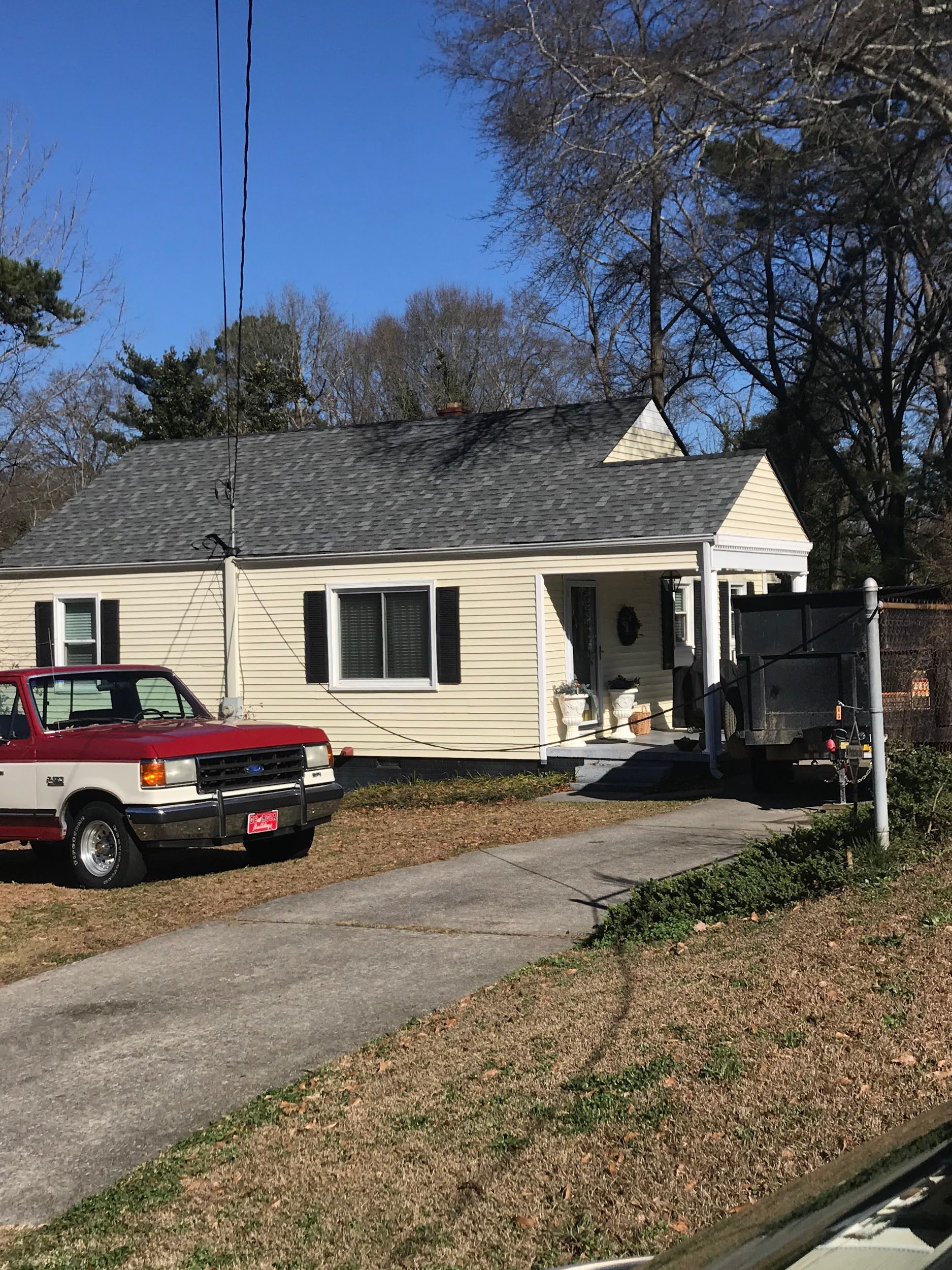 A small, cream-colored house with a red and white pickup truck parked in the driveway.