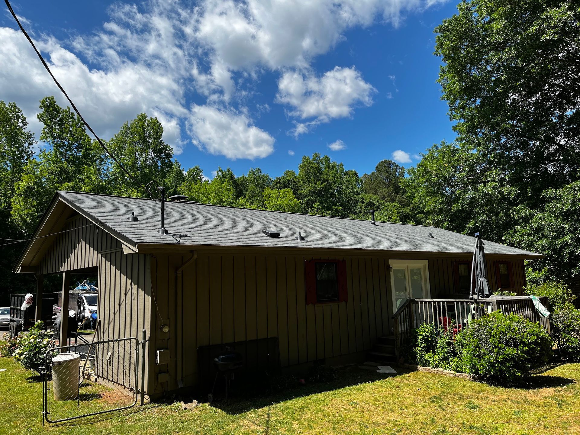 Brown house with gray roof and porch against a blue sky with clouds and green trees.