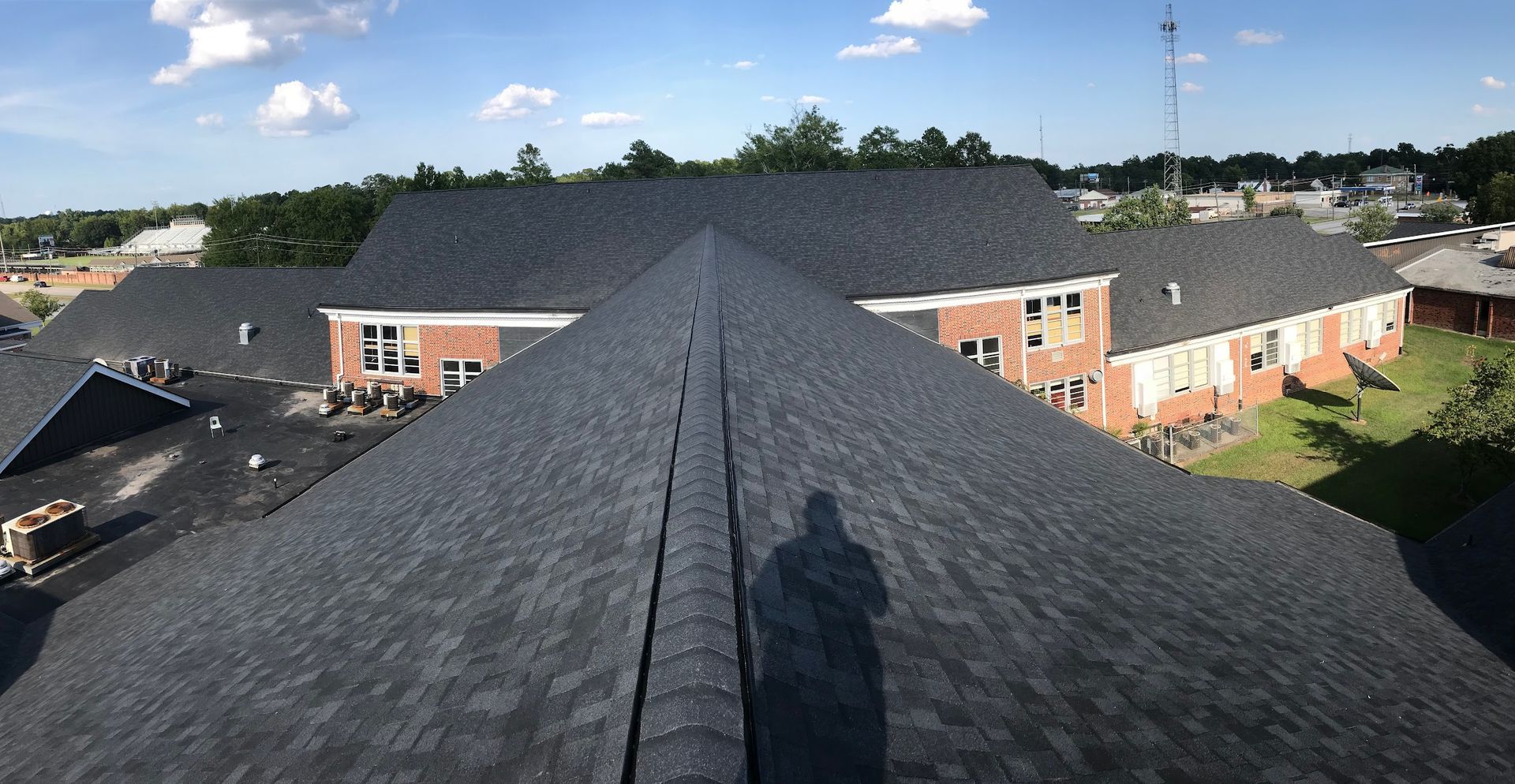 Aerial view of a dark shingled roof on a brick building under a blue sky.