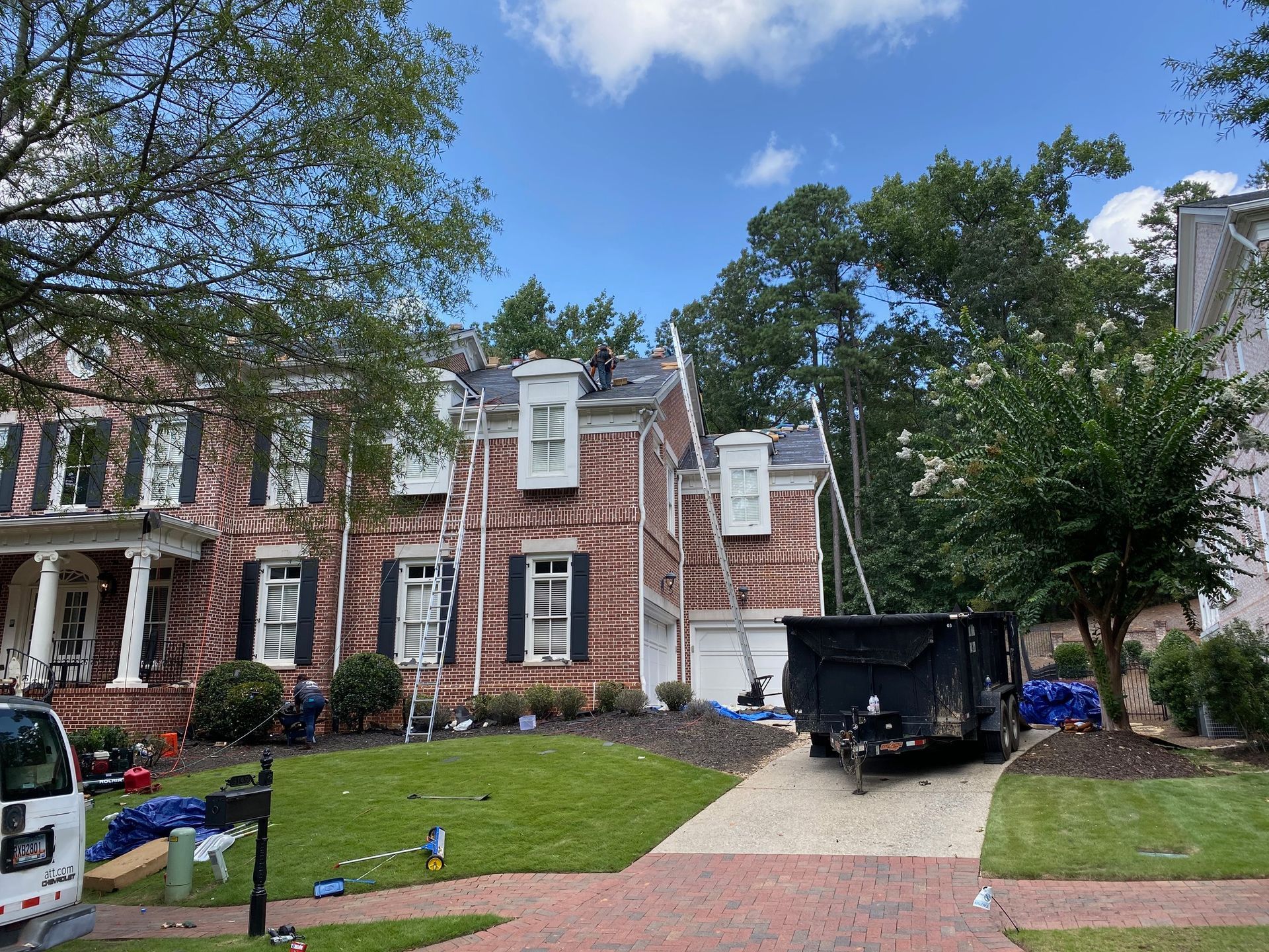 House with workers on the roof, ladders, and a dumpster on the driveway for a roofing project.