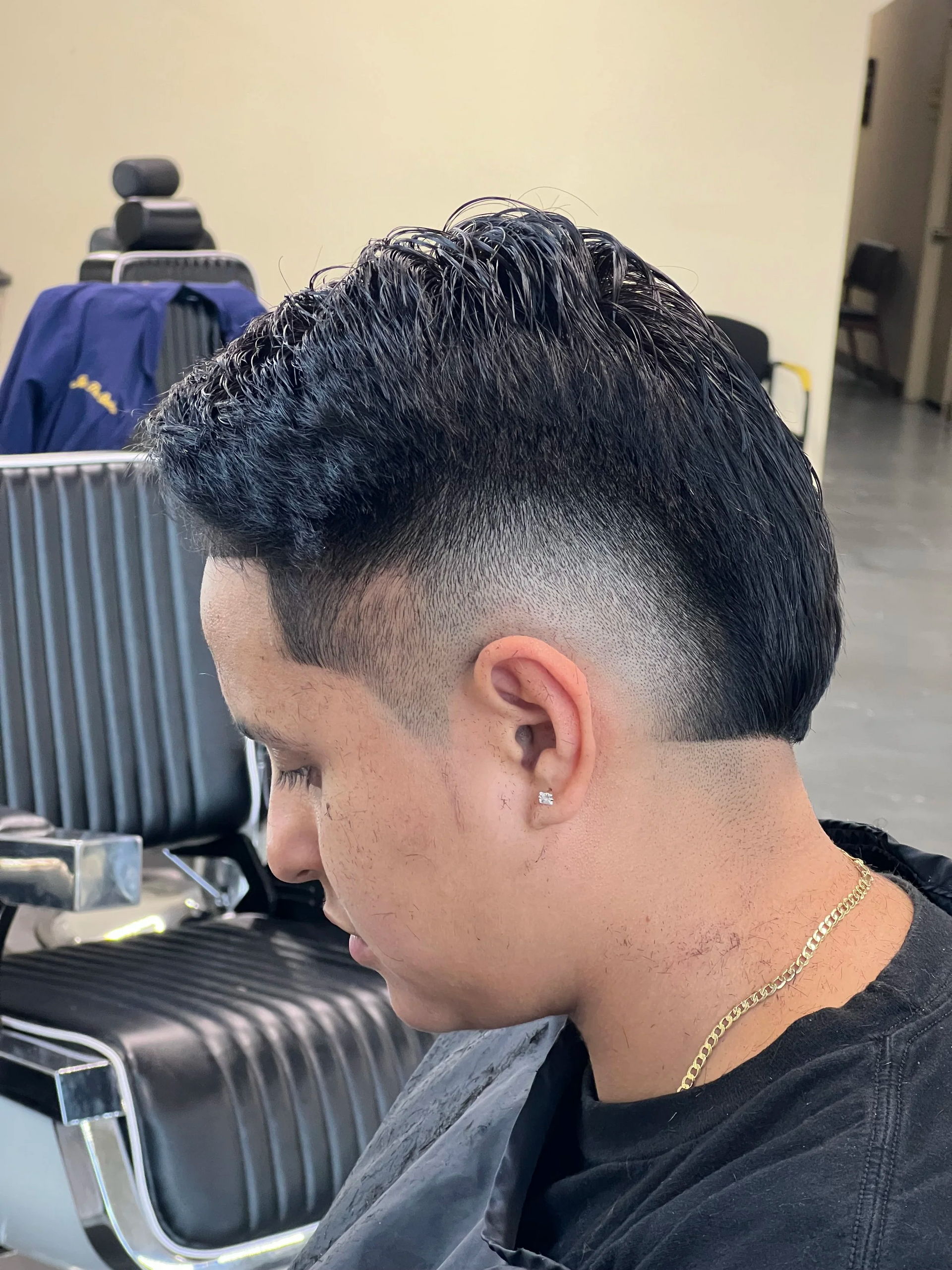 A side view of a person with a short, textured mohawk and a faded haircut, sitting in a salon chair.