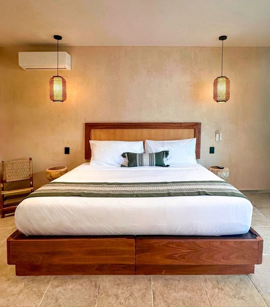 Bedroom with a wooden bed, woven headboard, white bedding, green runner, and pendant lights.