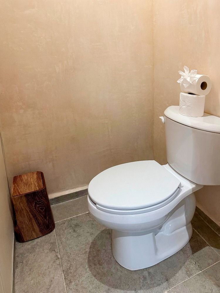 White toilet in a small bathroom with a wood stool and two rolls of toilet paper on the tank.