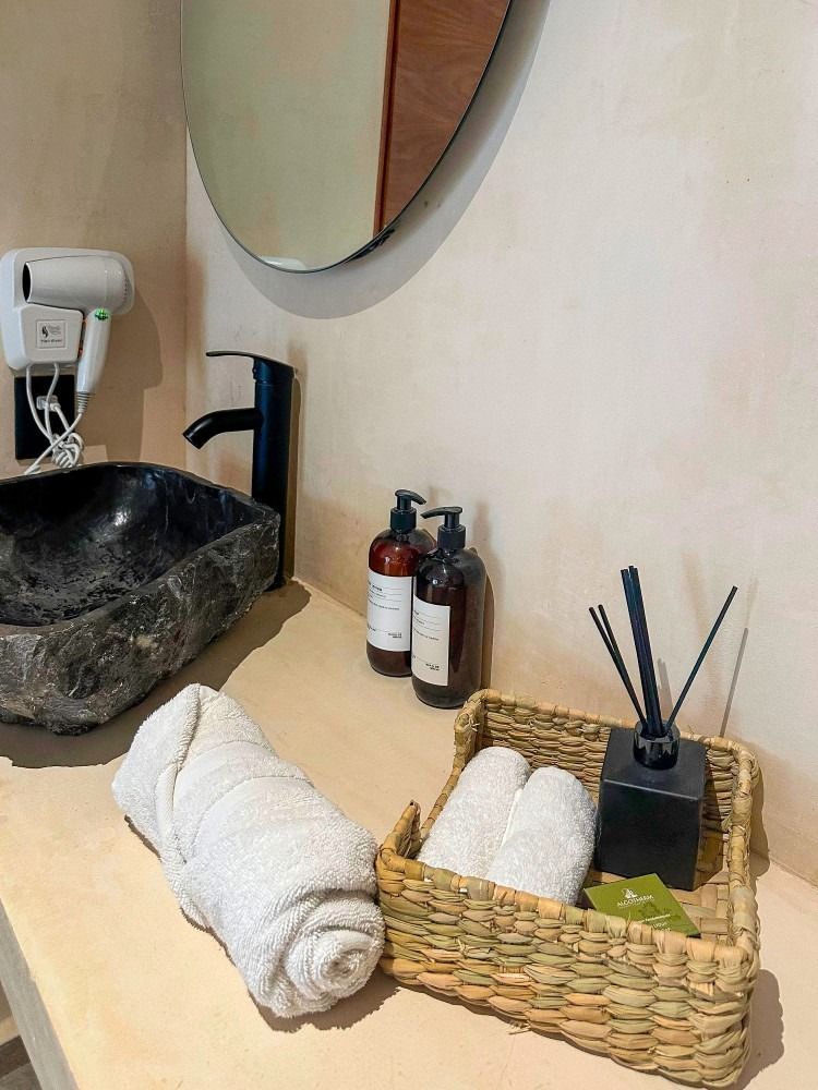 Bathroom vanity with a dark stone sink, black faucet, toiletries, towels, and a mirror.