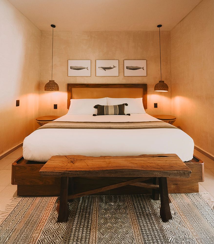 Bedroom with a wooden bed, woven headboard, white bedding, green runner, and pendant lights.