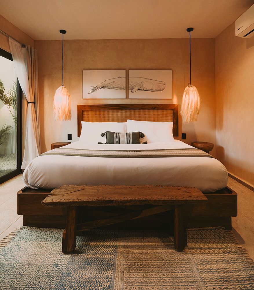 Bedroom with a bed, two pendant lights, and a side table. Neutral walls, wooden accents, and a green bed runner.
