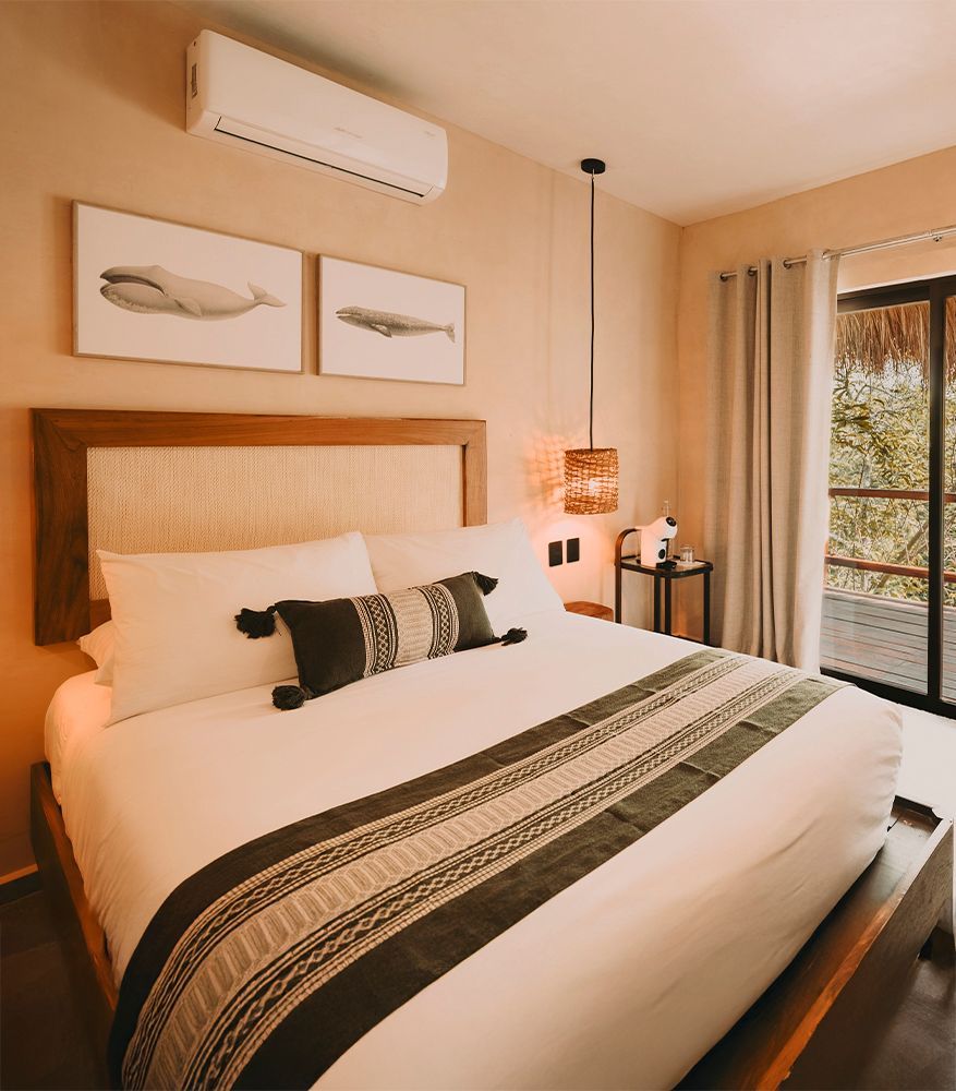 Bedroom with a wooden bed frame, rattan headboard and pendant lights, beige walls, and white bedding.