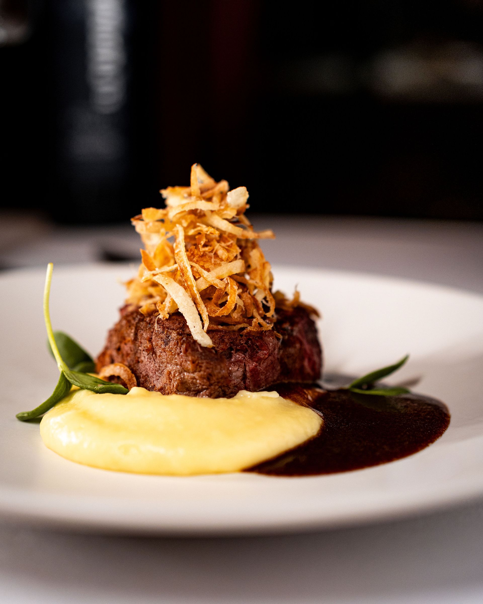 Plate of seared steak topped with fried onions, with mashed potatoes and dark sauce.