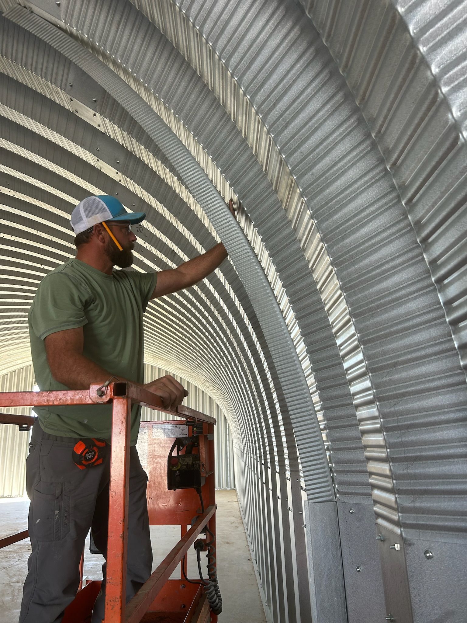 Man in lift, working on curved metal building interior.