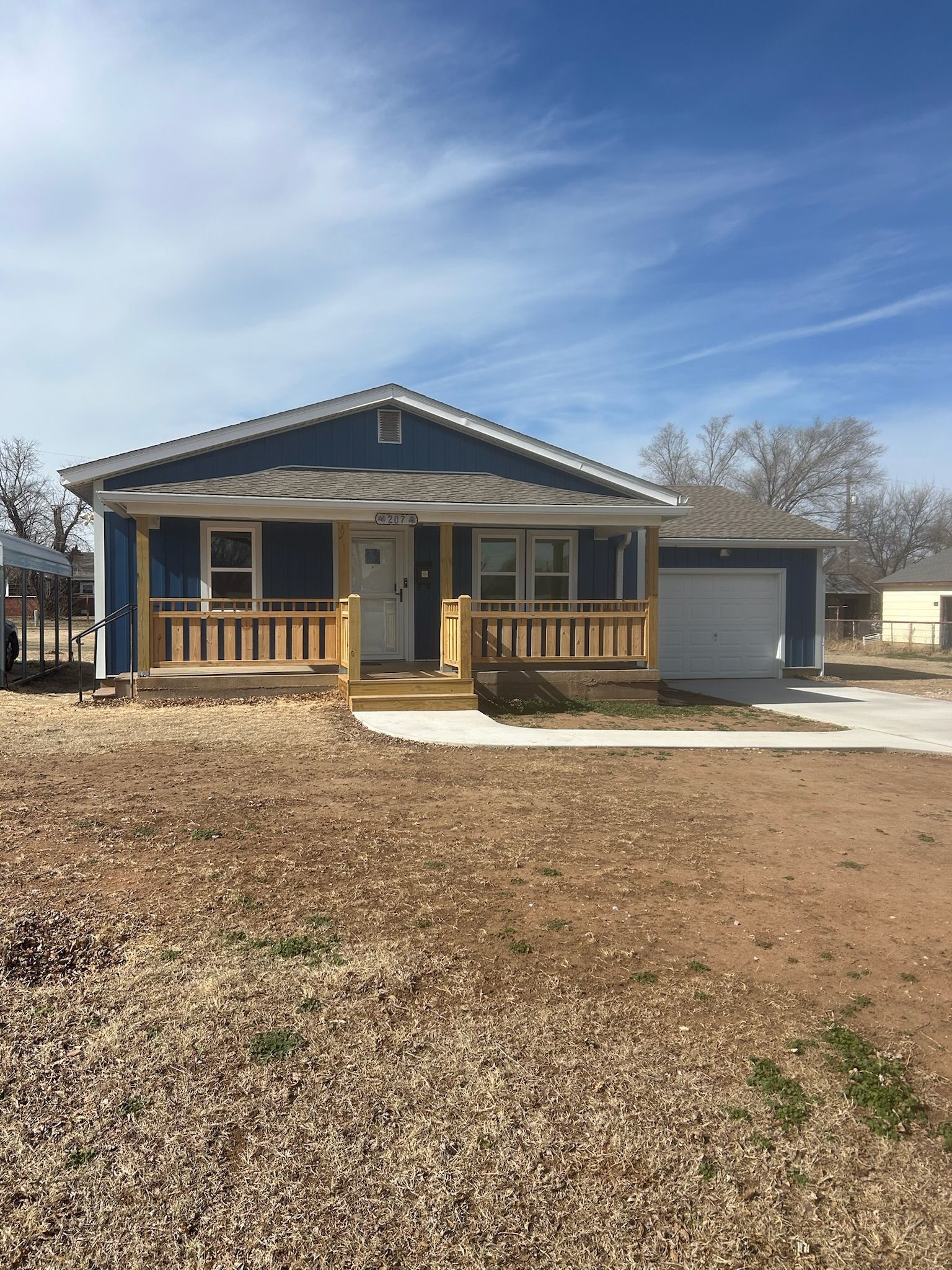 Blue house with wooden porch and attached garage on a sunny day.