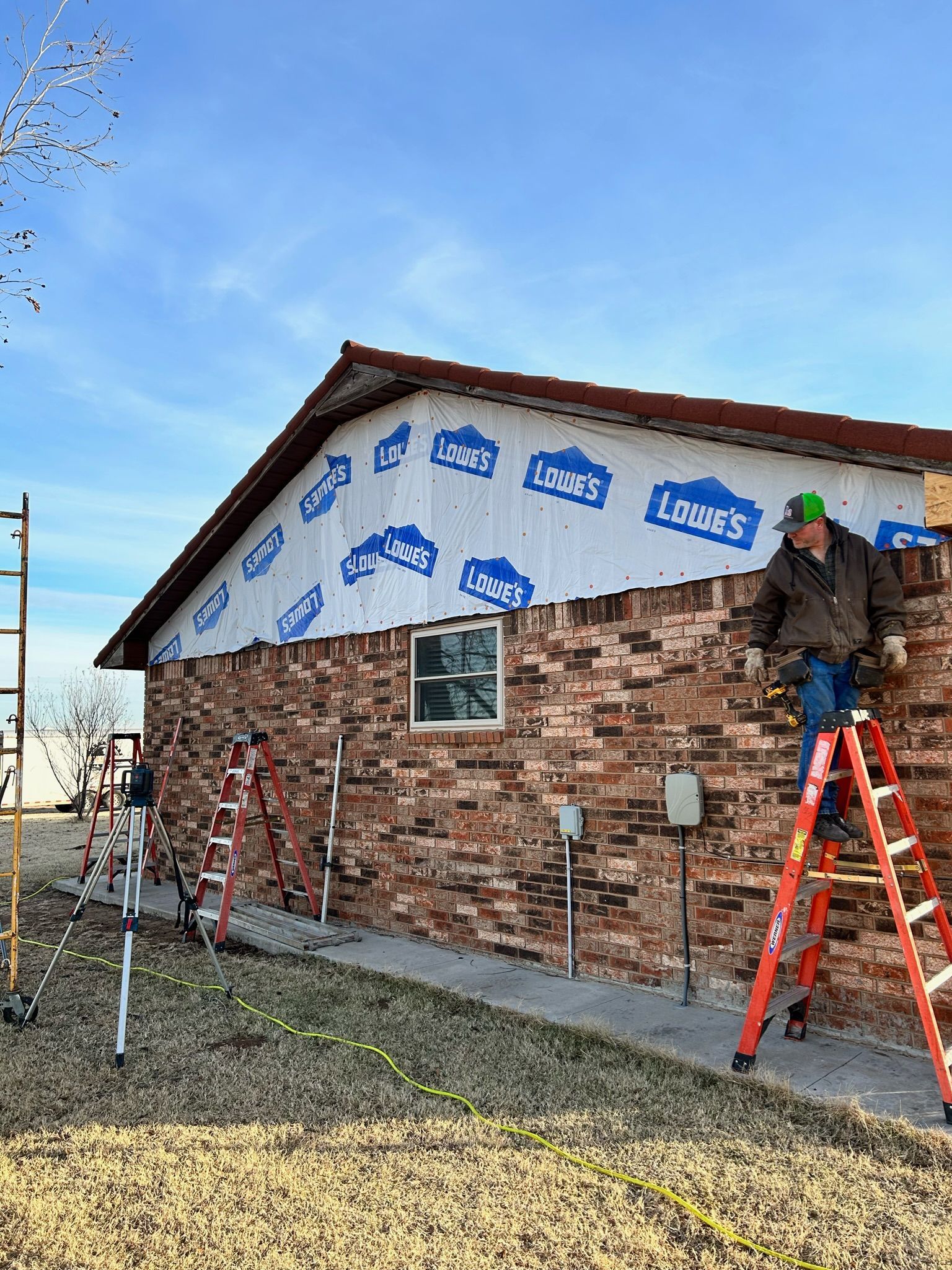 Man on ladder laying brick siding on building exterior with blue Lowe's wrap.