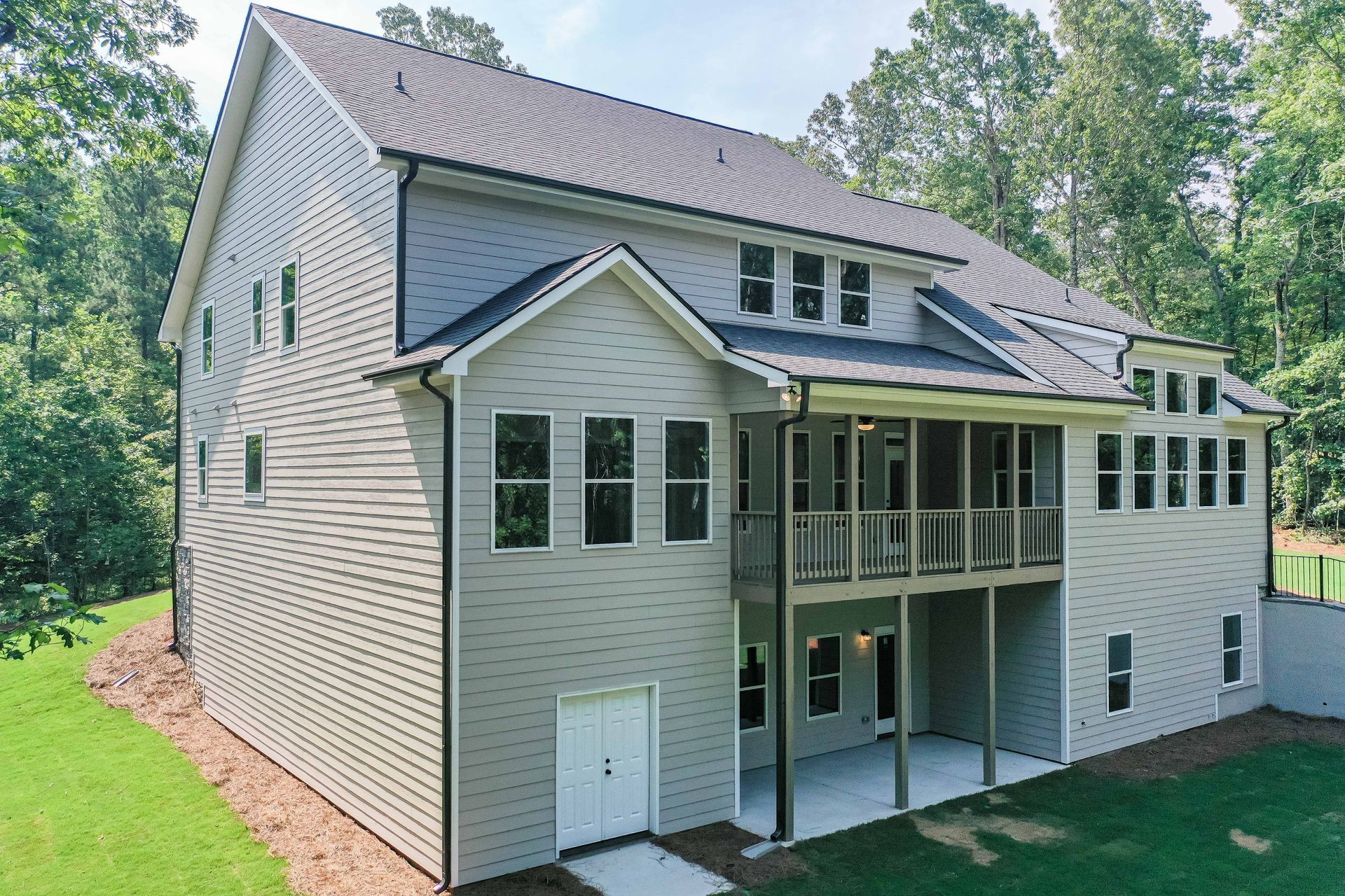 Two-story gray house with multiple windows, a screened porch, and a white garage door, set in a wooded area.