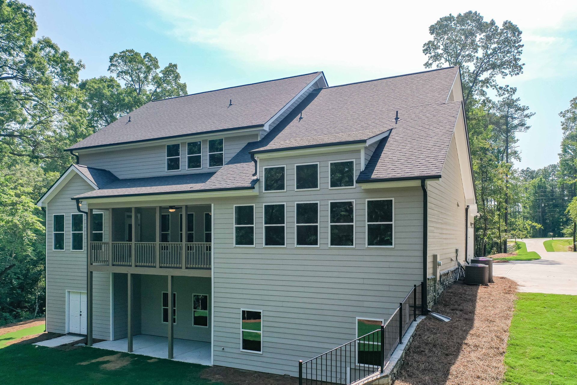 Two-story house with light siding and dark roof, screen porch, surrounded by trees and grass.