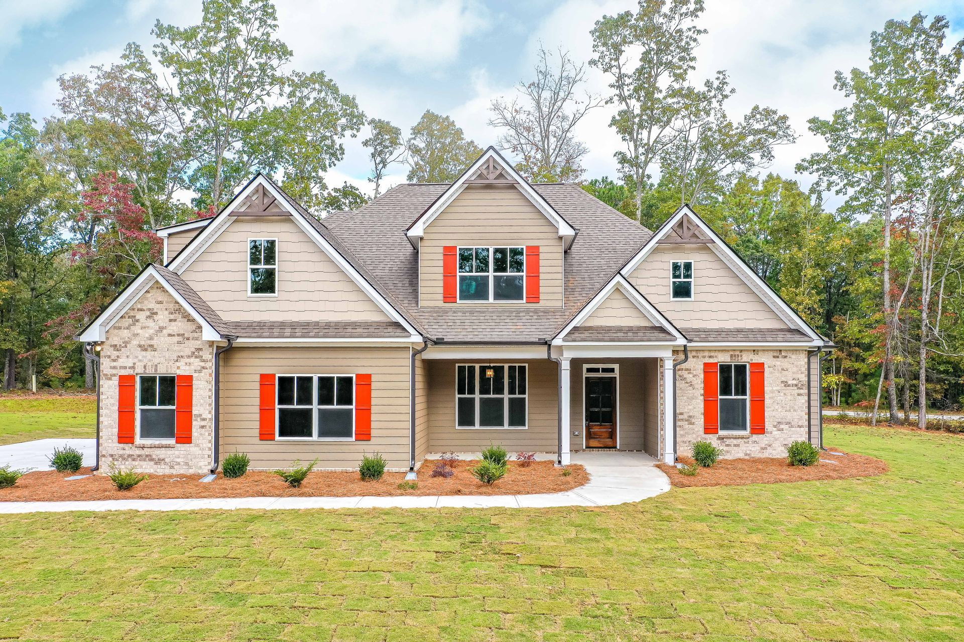 Tan and brick house with orange shutters, on a green lawn with trees in background.